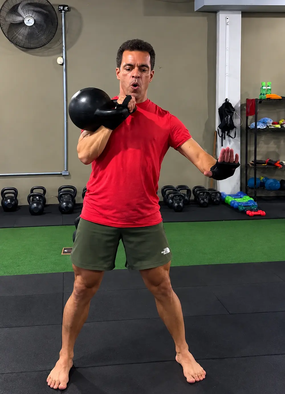 Aluno segurando o kettlebell junto ao peito, com a parede de kettlebells ao fundo